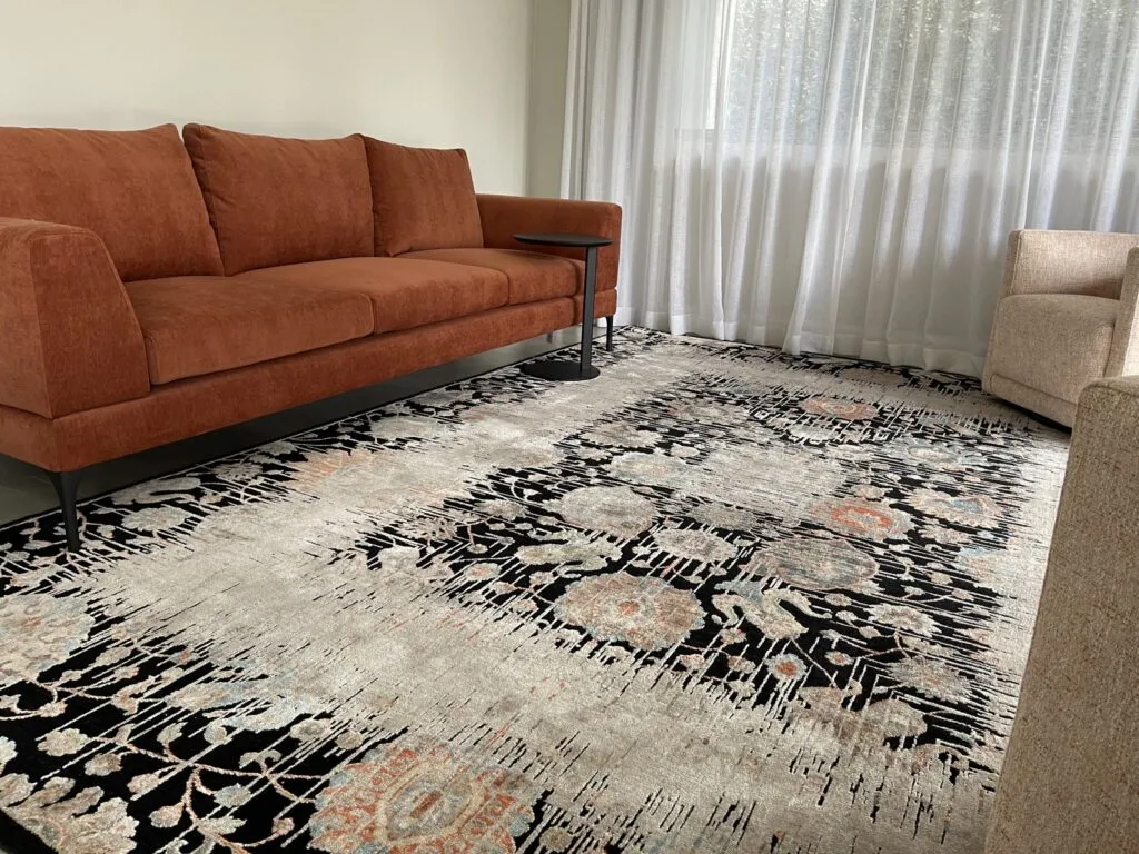 Black and ivory floral rug in front of a rust sofa