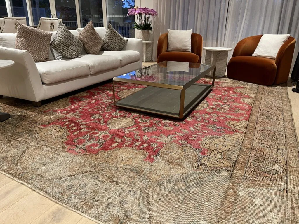 Red Persian rug under a glass coffee table, with a cream sofa and rust armchairs