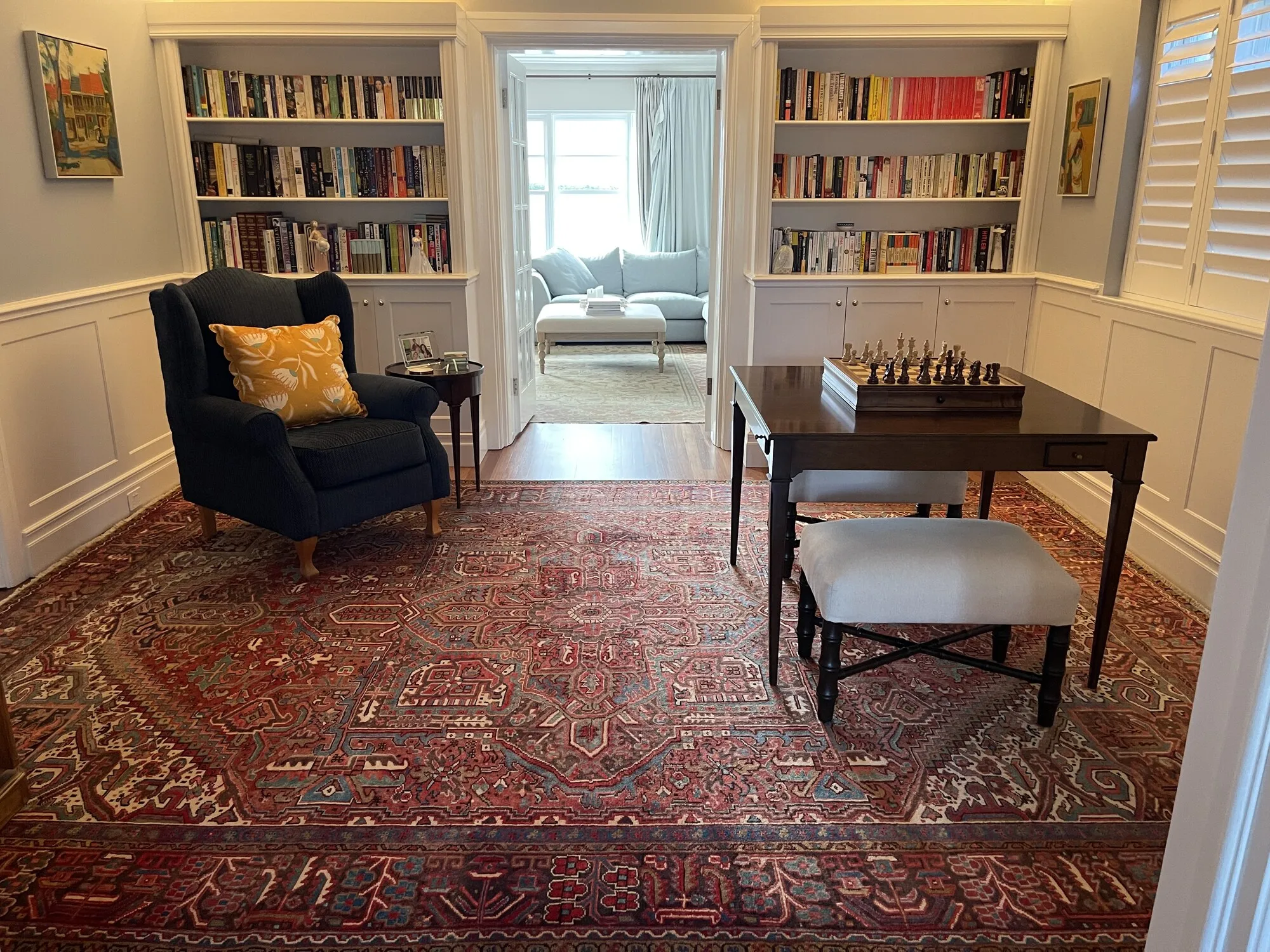 A red hand-knotted Persian rug under a reading chair and chess table in a client's library
