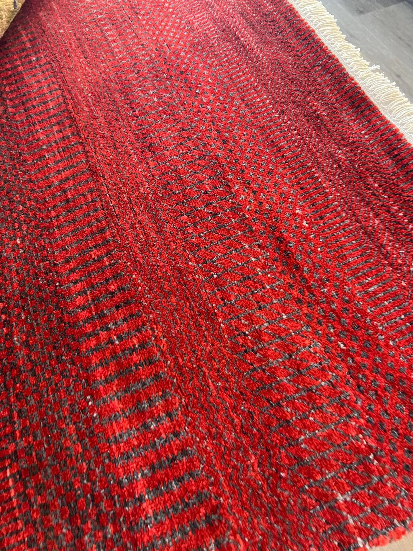 Close-up of a red hand-knotted rug with a fine dark pattern, on the showroom floor